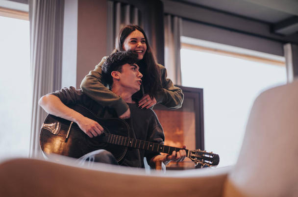 Ρομαντική στιγμή ως ένα ζευγάρι που αγαπά παίζει κιθάρα μαζί σε ένα άνετο περιβάλλον στο σπίτι. - Φωτογραφία, εικόνα