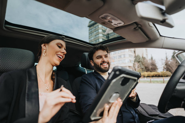 Profesyonel bir erkek ve kadın bir arabanın arka koltuğunda birlikte güler, tabletin içeriğini paylaşırlar.. - Fotoğraf, Görsel
