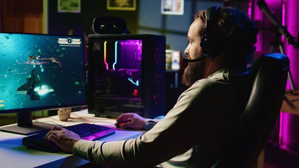 Mies neon valaistu asunto hauskaa ja nauraa pelatessaan viihdyttävä videopeli online-ystäviä, lentävät avaruusalus kautta galaksin yhdessä ja kommunikoida kuulokkeiden mikrofoni - Valokuva, kuva