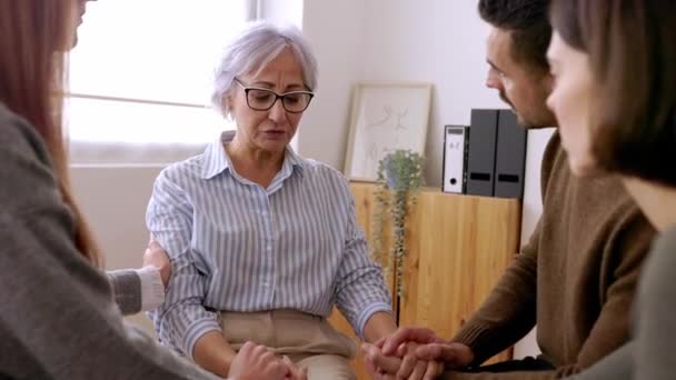 Diverse people sitting in circle receiving support during a therapy session. Young adult man and woman calming depressed senior woman partner in professional guidance meeting.  - Filmagem, Vídeo
