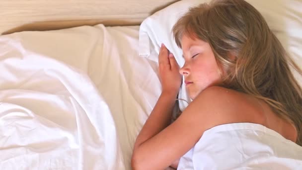 Mała dziewczynka z długimi włosami spokojnie śpi rano w wygodnym łóżku na białej poduszce. Zamknij slow motion top view clip.It idealny do projektów związanych z rodziną, dzieciństwem, lub - Materiał filmowy, wideo