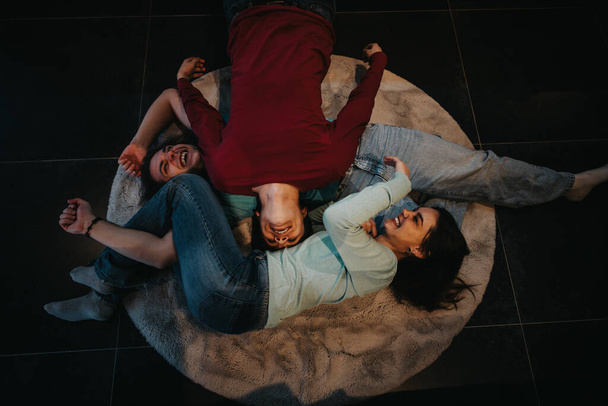 Top view of cheerful friends lying down on a soft rug, enjoying quality time and sharing a hearty laugh. - Photo, Image