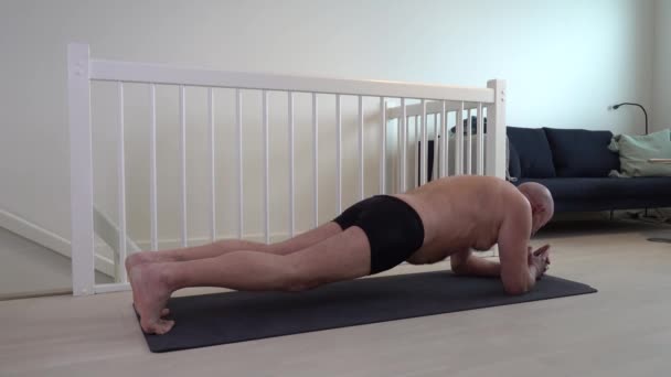 Muž středního věku dělá své každodenní cvičení rutiny na podložce na jógu doma.  - Záběry, video
