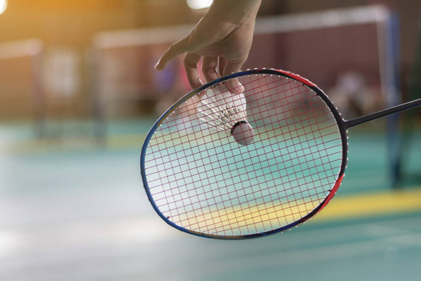 El jugador de bádminton sostiene la raqueta y el volante de crema blanca frente a la red antes de servirlo en otro lado de la cancha - Foto, imagen