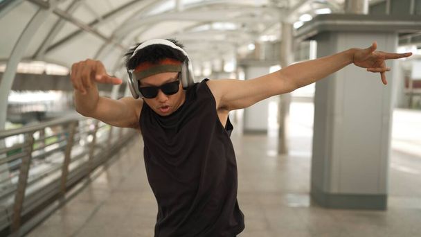 Close-up de dançarino bonito inteligente movendo as mãos enquanto dança a música hip hop. Asiático hipster usando fone de ouvido enquanto caminha ao longo do corredor com fundo borrado. Desporto ao ar livre 2024. Sprightly. - Foto, Imagem