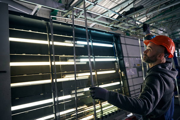 Man with a beard glues spacer frames at a window production facility, a man in an orange helmet - Foto, imagen