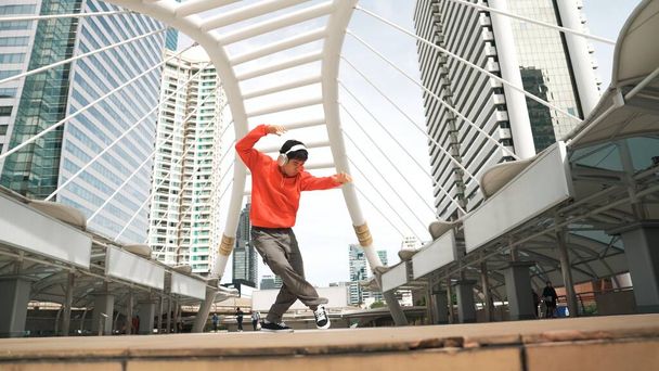 Azjatycki hipster w słuchawkach pokazuje kroki podczas skakania po mieście. Profesjonalny tancerz break dance b-boy w mieście. Break dance albo street dance. Sport na świeżym powietrzu 2024. Sprytnie. - Zdjęcie, obraz