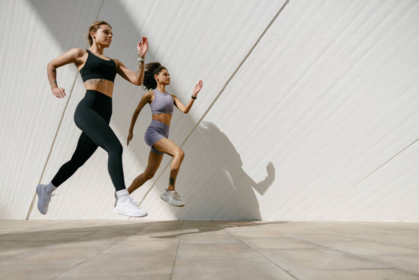 Két aktív női sportoló fut egymás mellett egy szabadtéri pályán a modern épületek hátterében - Fotó, kép