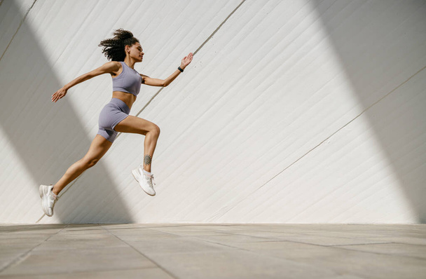 Fit mujer atleta en ropa deportiva se está ejecutando en los edificios modernos de fondo. Concepto de estilo activo - Foto, imagen
