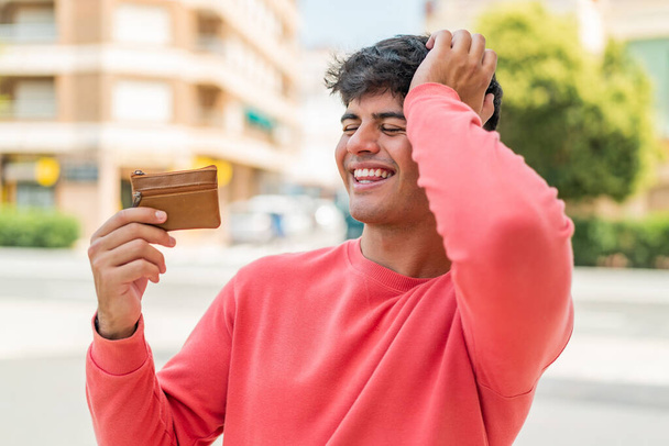 Молодой латиноамериканец, держащий бумажник на улице, кое-что понял и намеревается решить - Фото, изображение