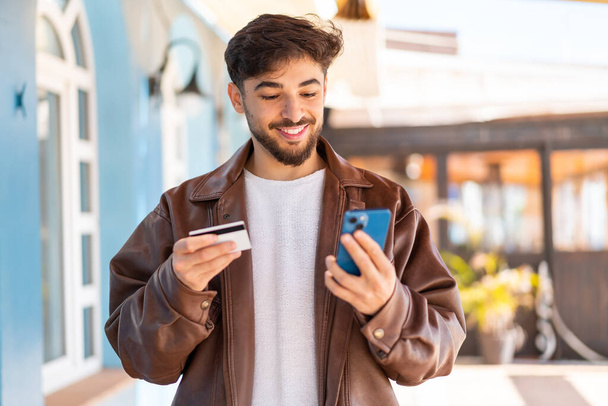 Schöner arabischer Mann beim Outdoor-Kauf mit dem Handy und Kreditkarte - Foto, Bild