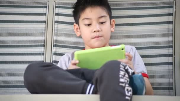 Ładny chłopiec azjatyckich gry komputera typu tablet w parku w dzień jasny lato - Materiał filmowy, wideo