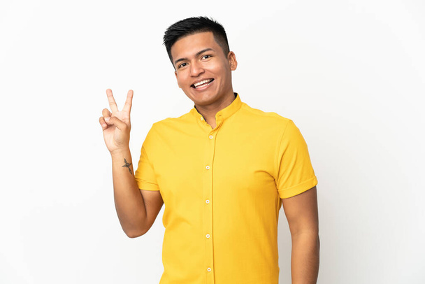 Mladý ekvádorský muž izolovaný na bílém pozadí s úsměvem a ukazující znamení vítězství - Fotografie, Obrázek