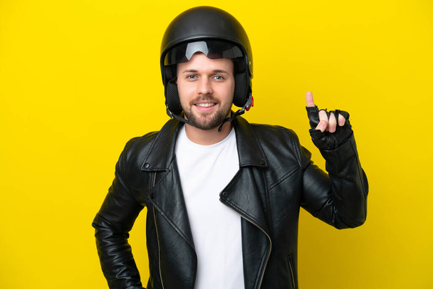 Joven hombre caucásico con casco de moto aislado sobre fondo amarillo apuntando a una gran idea - Foto, Imagen