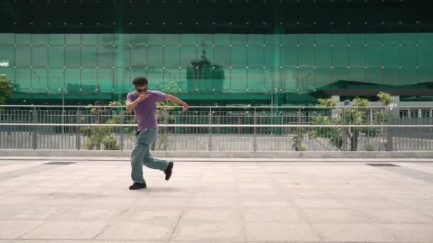 Ázsiai hipszter megdermedt pózban, miközben a kamerát nézte a városban. Panoráma lövés a profi utcai táncos gyakorlat b-fiú lépés vagy break tánc. Modern életmód.Kültéri sport 2024. Élénk.. - Felvétel, videó