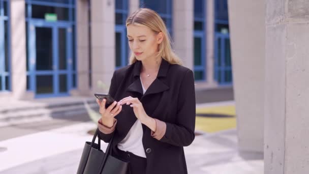 Glimlachende zakenvrouw met een handtas aan het praten op een mobiele telefoon buiten een kantoorgebouw. - Video