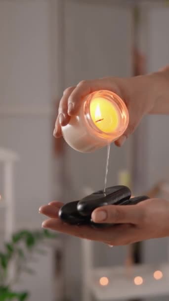 A massage therapist in a massage spa salon prepares for massage therapy with hot stones by pouring special aroma massage oil from a candle over them. A magical atmosphere of relaxation and relaxation - Footage, Video