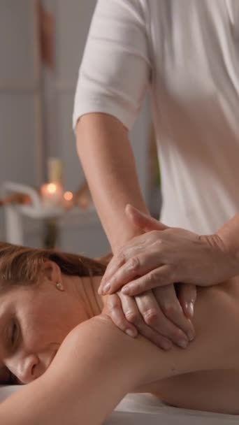 Die Frau liegt entspannt auf dem Massagetisch, während der Masseur sanft an Rücken und Schultern arbeitet und verschiedene Techniken anwendet, um die Muskeln zu entspannen und die Durchblutung zu verbessern. Schultermassage. Hohe Qualität 4k - Filmmaterial, Video
