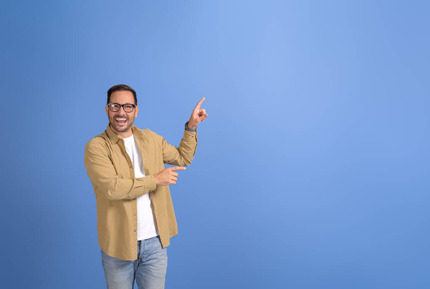 Portret młodego biznesmena śmiejącego się i celującego w przestrzeń do kopiowania reklam na niebieskim tle - Zdjęcie, obraz