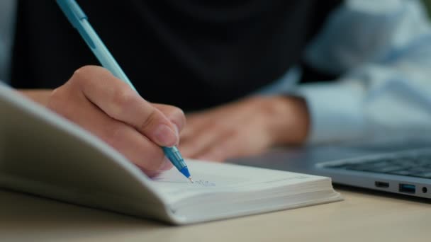 Крупним планом жіноча рука пише в блокноті невпізнавана бізнес-леді ісламська жінка в хіджабі студентка, яка вивчає написання нотаток завдання бізнес-документація фінансовий бюджет з ноутбуком на офісному столі - Кадри, відео