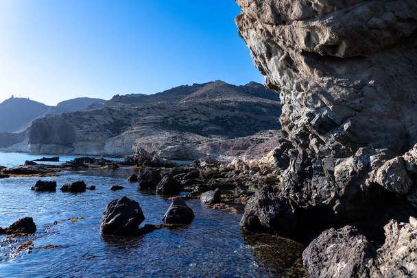 Cabo de Gata, Almeria - Espanja - 01-23-2024: Silhouetoidut kalliomuodostelmat ja kuohuva meri Cabo de Gatan kirkkaassa auringonvalossa - Valokuva, kuva