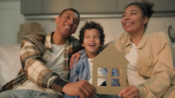 Happy African American family mom dad son kid boy child hold little cardboard house frame in hands together symbol dream home moving day relocation buying new flat real estate insurance loan mortgage - Footage, Video