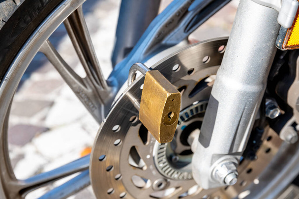 Treviso, Venetien - Italië - 06-08-2021: Een close-up van een fiets- of motorschijfrem beveiligd met een stevig hangslot, symbool voor de veiligheid van stadsvoertuigen - Foto, afbeelding