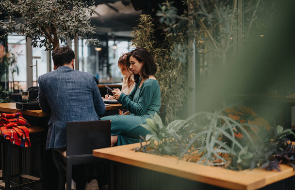 Három szakember vett részt egy startup üzleti találkozón egy modern városi kávézóban, ahol digitális táblagépek és notebookok mellett tárgyaltak.. - Fotó, kép