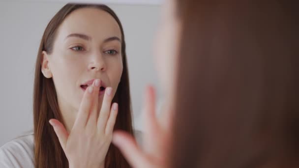 Eine junge erwachsene Frau untersucht ihr Spiegelbild und konzentriert sich dabei auf Hautpflege und Schönheit im häuslichen Umfeld. - Filmmaterial, Video