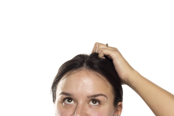 half portret van een jonge vrouw op zoek omhoog en sctratching haar hoofd op een witte studio achtergrond - Foto, afbeelding