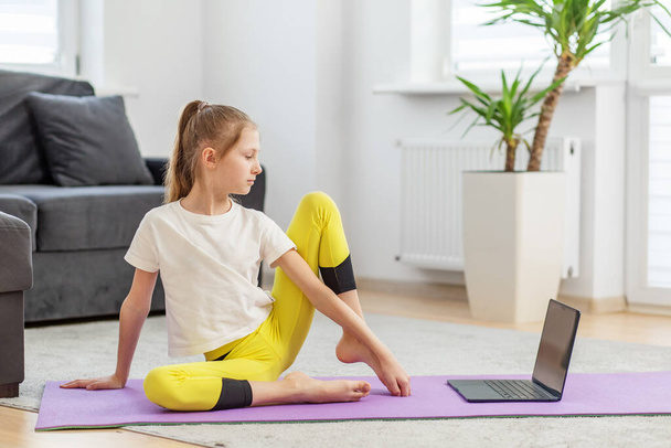 Chica concentrada en la torsión de la postura de yoga mira a un ordenador portátil, participar en clases de yoga virtual en casa. - Foto, Imagen