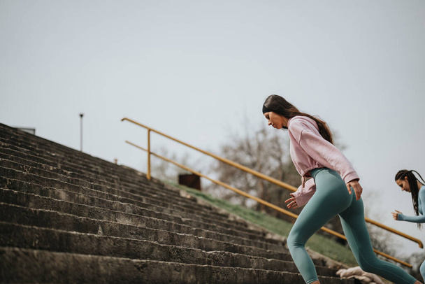 Dos mujeres activas en ropa deportiva corriendo escaleras al aire libre, centrándose en la aptitud y un estilo de vida activo. - Foto, imagen