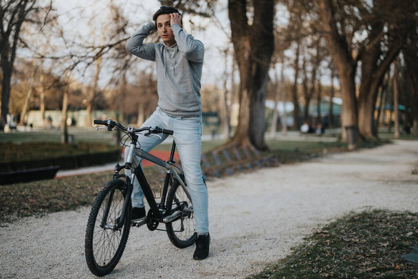 穏やかな公園の環境で静けさの瞬間を楽しむために自転車に乗る間に思慮深い男が休む. - 写真・画像