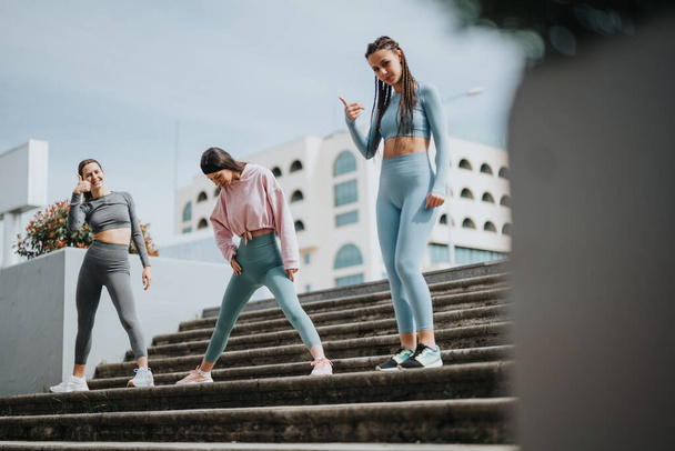 Drei junge Frauen strecken sich in Fitnessbekleidung auf Stufen im Freien und zeigen einen gesunden Lebensstil. - Foto, Bild