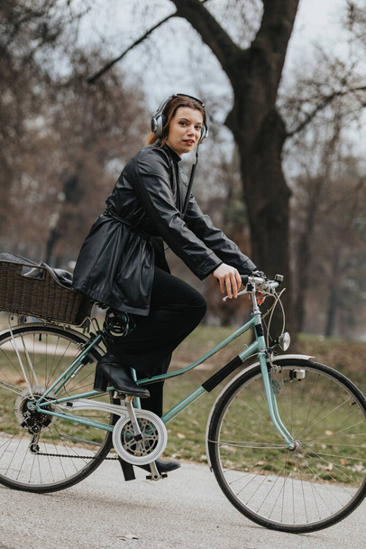 Jeune femme confiante et élégante profitant d'une balade à vélo dans le parc avec des écouteurs classiques. - Photo, image