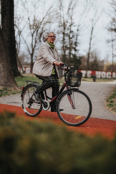 Maduro feminino aposentado sorrindo enquanto pedalava ao ar livre, retratando um estilo de vida ativo e independência. - Foto, Imagem