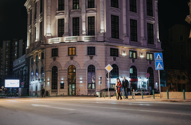 Ένα κομψό επιχειρηματίες απολαμβάνει μια βραδινή βόλτα σε ένα δρόμο της πόλης, φωτίζεται από τα φώτα μιας μεγάλης ιστορικής αρχιτεκτονικής και λάμψη της πόλης. - Φωτογραφία, εικόνα
