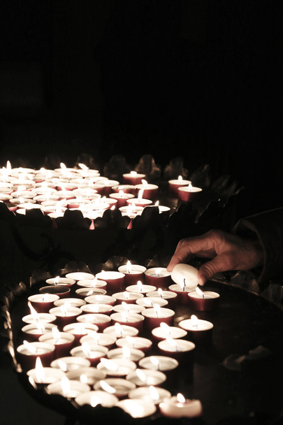 Рука пожилой женщины зажигает свечу в память о погибших
 - Фото, изображение