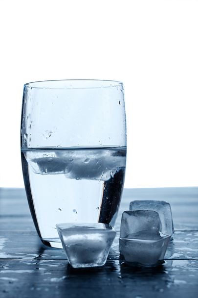 Glas water en smeltende ijsblokjes op een houten tafel. - Foto, afbeelding