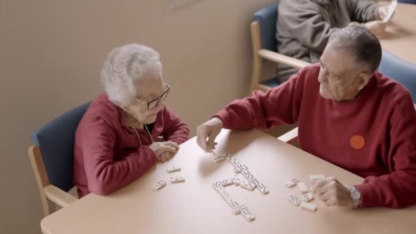 slow motion video van een senior man spelen dominostenen met oude vriend in een geriatrische - Video