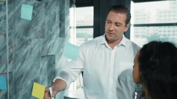 Skilled businessman presents marketing idea to project manager by using colorful sticky notes at glass wall. Project manager pointing, explaining, showing start up project to investor. Manipulator. - Footage, Video