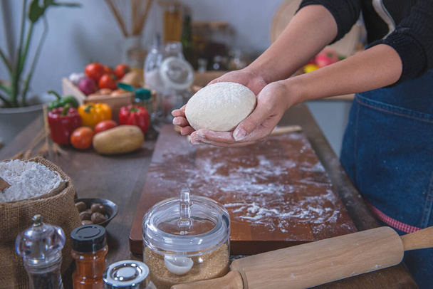 Η γυναίκα χρησιμοποιεί τα χέρια για να ζυμώσει τη ζύμη πίτσας, προετοιμάζει και ξεκουράζει τη ζύμη πίτσας πριν την βάλει στο φούρνο. Στην ιδέα της κουζίνας και σπιτική πίτσα - Φωτογραφία, εικόνα