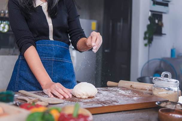 Nainen seisoo keittiössä käyttäen käsiään ripottelemaan jauhoja. joka on prosessi tehdä pizzaa ruokaa käsitteitä ja kotitekoinen pizza - Valokuva, kuva