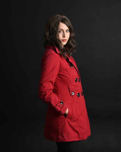 primo piano ritratto di bella modella donna bruna, indossando trench rosso cappotto.isolato su sfondo scuro studio con ombre. mani nelle tasche della giacca. - Foto, immagini