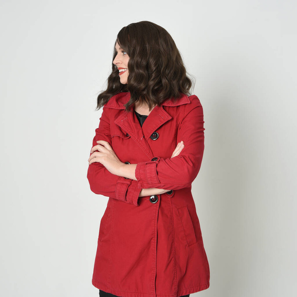 Kopf und Schultern aus nächster Nähe Porträt der schönen brünetten Frau Modell, trägt rote Trenchcoat-Jacke. isoliert auf weißem Studiohintergrund. Arme in selbstbewusster Geste verschränkt. - Foto, Bild