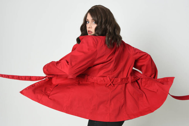 close-up portret van mooie brunette vrouw model, het dragen van rode trench jas jacket.isolated op witte studio achtergrond. poseren met achteraanzicht, weg draaien van de camera. - Foto, afbeelding
