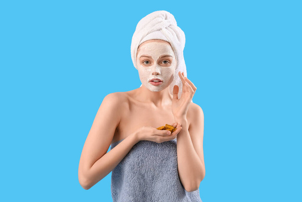 Νεαρή γυναίκα με εφαρμοσμένη κουρκουμά μάσκα και ρίζες σε μπλε φόντο - Φωτογραφία, εικόνα