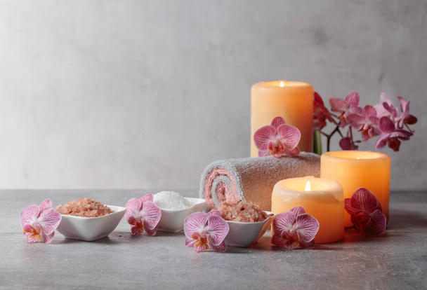 Sel marin, serviettes, fleurs d'orchidées et bougies allumées sur fond gris. Concept de spa avec espace de copie. - Photo, image