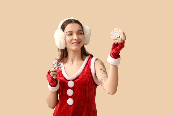 Schöne junge Frau als Weihnachtsmann gekleidet mit dekorativen Schneeflocken auf beigem Hintergrund - Foto, Bild