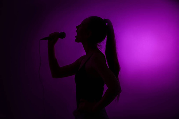 Силуэт женщины с современным микрофоном, поющей на темном фоне - Фото, изображение